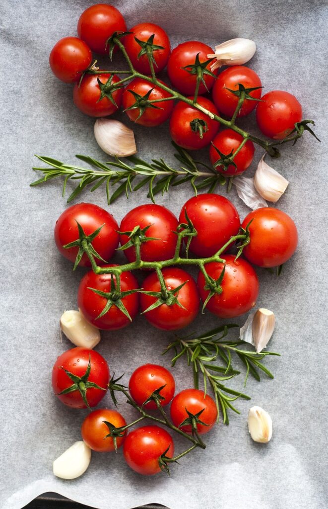 beste koolhydraatarme groenten. dire trossen tomaten met teenjtes knoflook op een tafel.