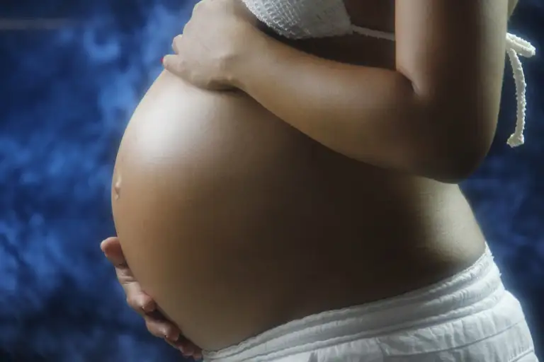 Afvallen na zwangerschap vrouw met handen op een zwangere buik.
