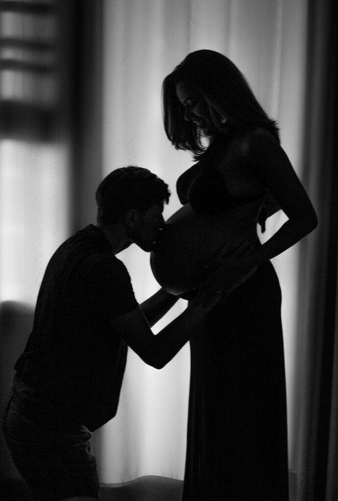 afvallen na zwangershap, silouet van een man die de zwangere buik van zijn vrouw kust.
