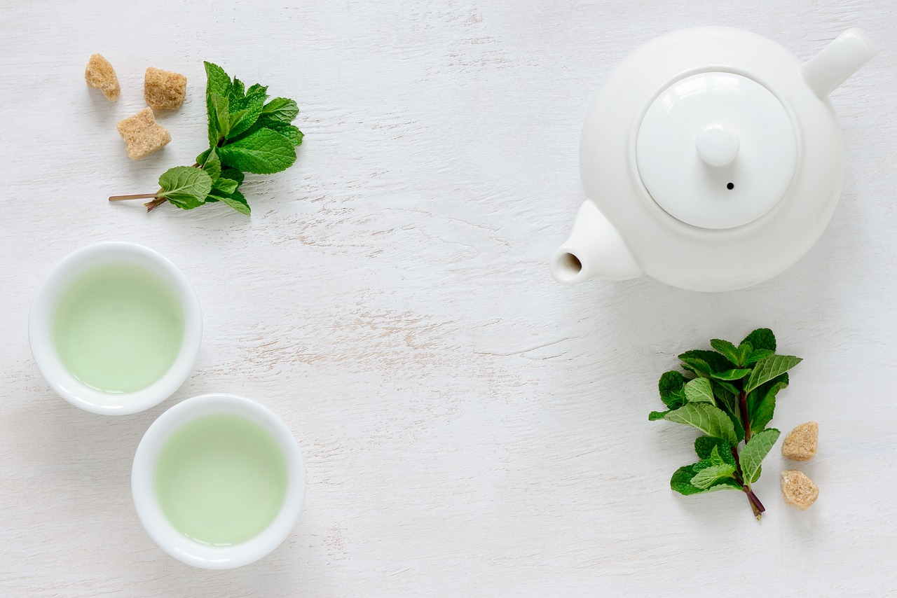 afvallen met groene thee- theepot met twee kopjes op een wiite tafel met losse blaadjes