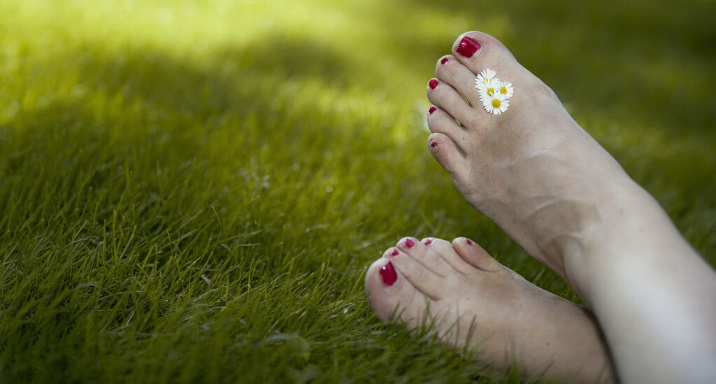 twee voeten met madeliefjes tussen de tenen in het grass.