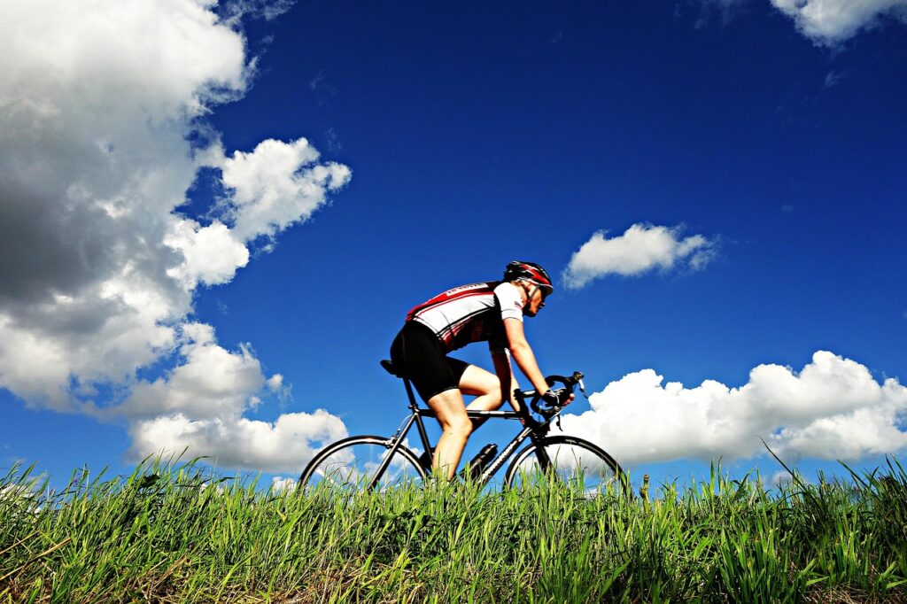 afvallen door fietsen - wielrenner voor het gras tegen een blauwe lucht met wolken