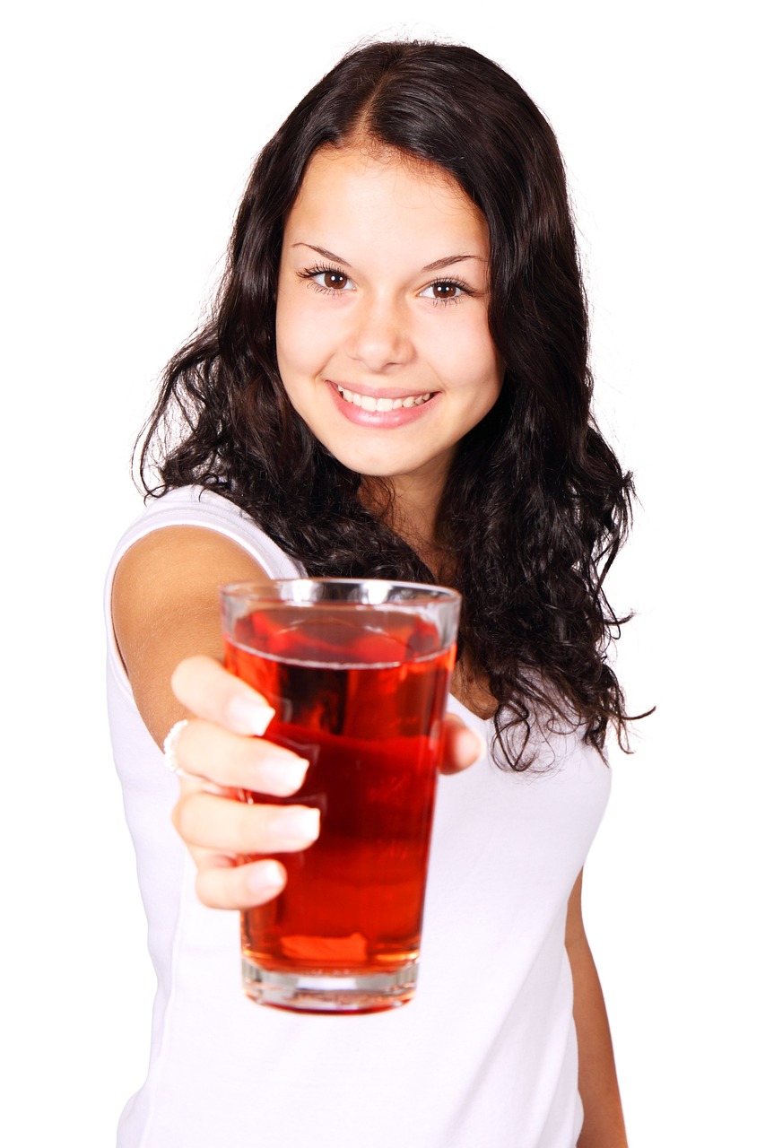 Vrouw met wit shirt en donker haar houdt een glas cranberriesap voor zich uit als alcohol vervanger