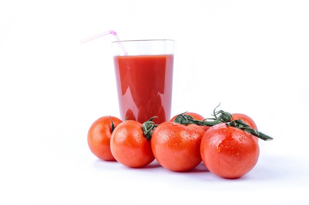 alcohol vervanger tomatensap in een glas achter vier rijpe tomaten.