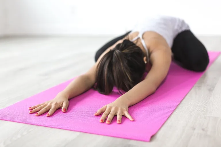afvallen met yoga, vrouw in yoga houding op een roze mat