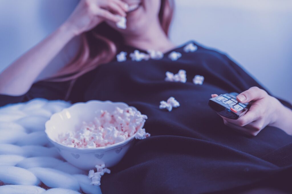 tips om  meer te bewegen, vrouw voor de tv met popcorn en afstandsbediening.
