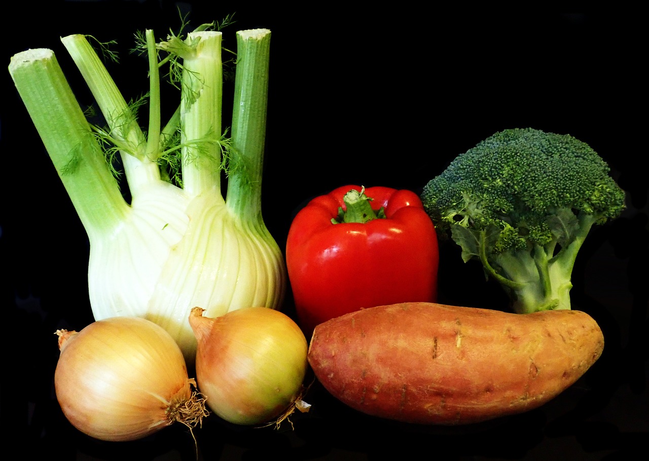 een Selderij, paprika, brocolli, uien en een zoete aardapel tegen een zwarte achtergrond.